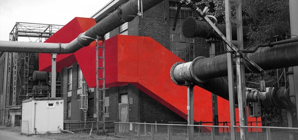 Ein beeindruckendes Industriegebäude mit einer großen, leuchtend roten Außentreppe ist von zahlreichen grauen und schwarzen Rohren und Metallstrukturen umgeben – das perfekte Motiv für eine Modeling Monday-Herausforderung mit Archicad.